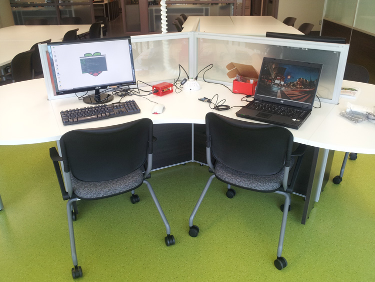 Image of two student work stations at the Sherman Centre. Each has desk space, a laptop, a chair. The floor is green.