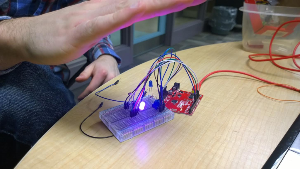 Image of a partially programmed smart night light. You can see exposed circuitry and wires. The light is glowing blue when covered by a hand, showing it is responding to the level of light it senses.