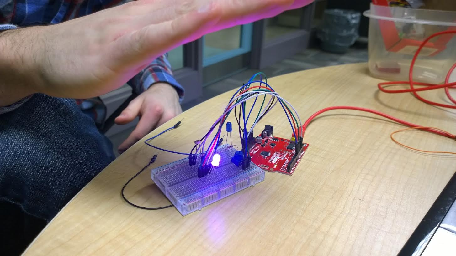 Image of a partially programmed smart night light. You can see exposed circuitry and wires. The light is glowing blue when covered by a hand, showing it is responding to the level of light it senses.